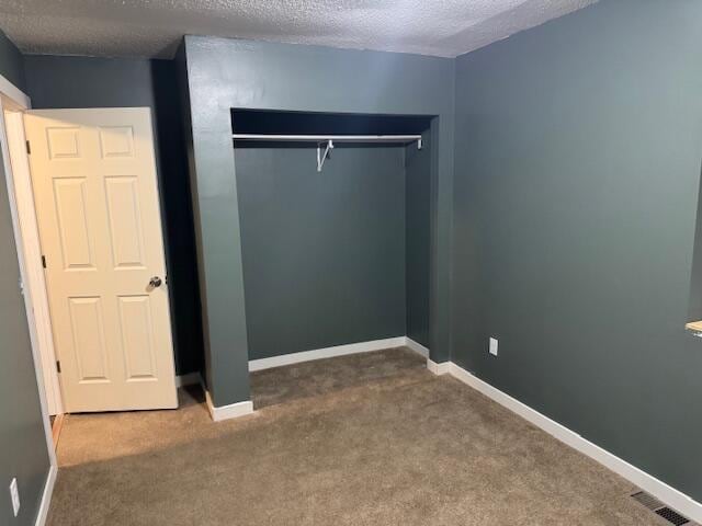 unfurnished bedroom with a textured ceiling, carpet floors, visible vents, and baseboards