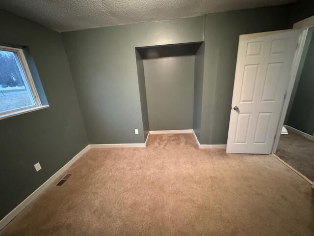 unfurnished bedroom with carpet floors, a textured ceiling, visible vents, and baseboards