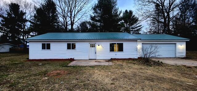 single story home featuring concrete driveway, an attached garage, a front yard, and metal roof