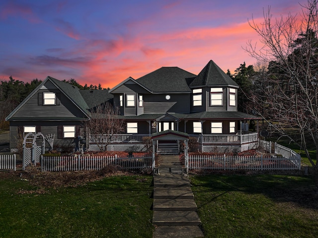 rear view of property featuring a lawn, a porch, a fenced front yard, and a shingled roof