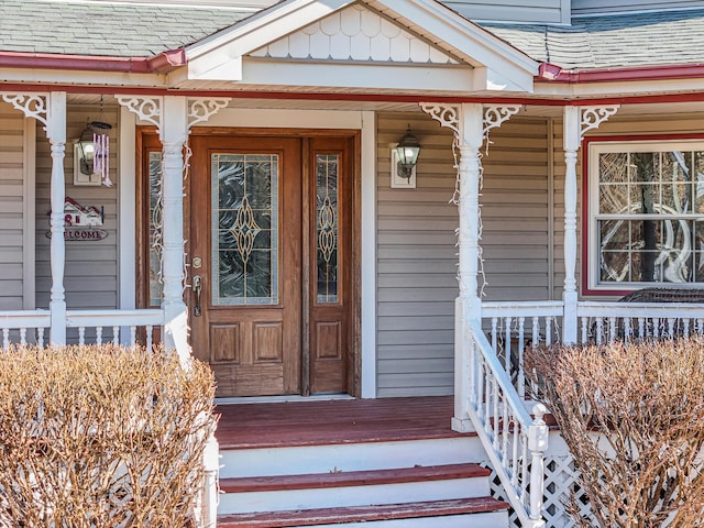 view of exterior entry with roof with shingles and a porch