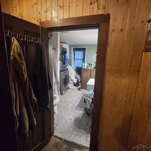 hall featuring stacked washer / drying machine and wooden walls