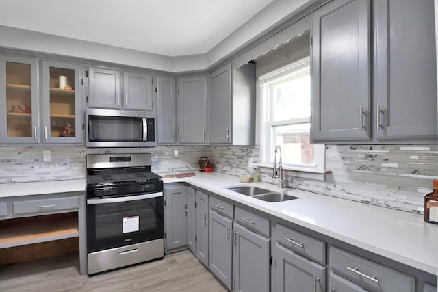 kitchen featuring stainless steel appliances, gray cabinetry, a sink, and decorative backsplash