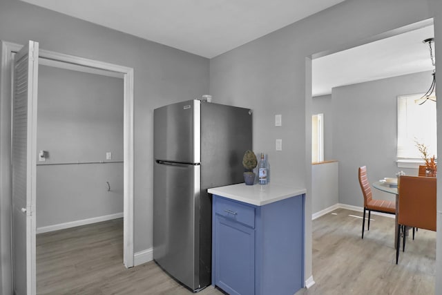 kitchen featuring freestanding refrigerator, light wood-style floors, blue cabinetry, light countertops, and baseboards