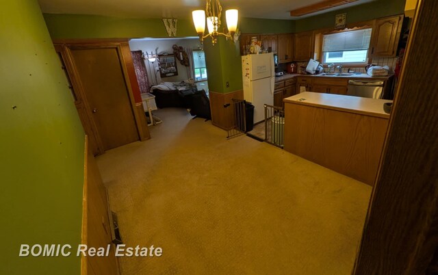 kitchen featuring freestanding refrigerator, a sink, stainless steel dishwasher, light colored carpet, and brown cabinetry