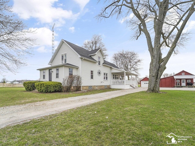 view of side of property with a porch, a detached garage, driveway, and a yard