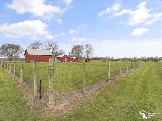 view of yard with fence, a rural view, a barn, and an outbuilding