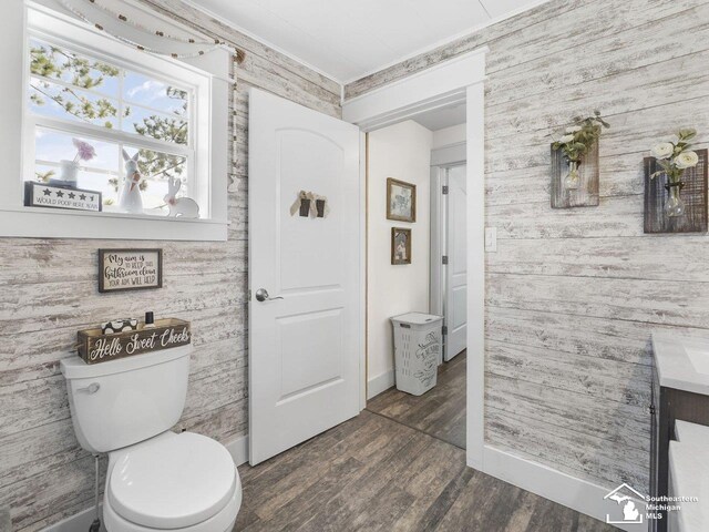 bathroom featuring toilet, wooden walls, wood finished floors, and baseboards