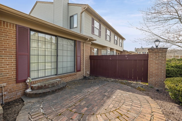 view of side of home with brick siding, fence, a patio, and a chimney