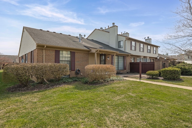 view of front of property featuring fence, roof with shingles, a front yard, and brick siding