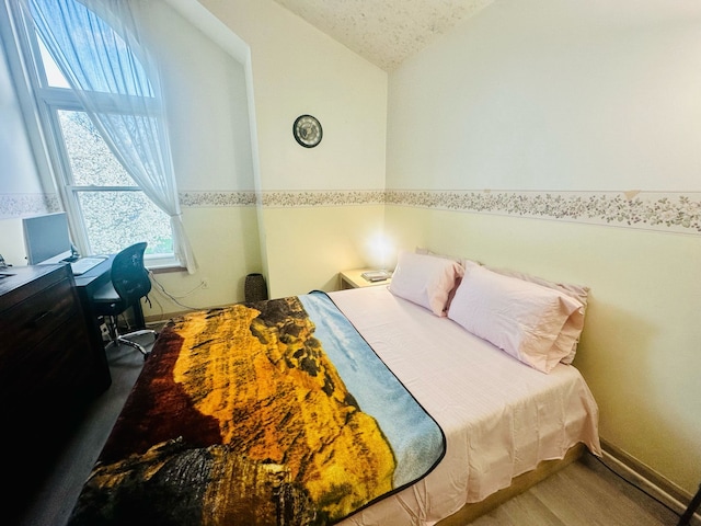 bedroom featuring wood finished floors, a textured ceiling, and lofted ceiling