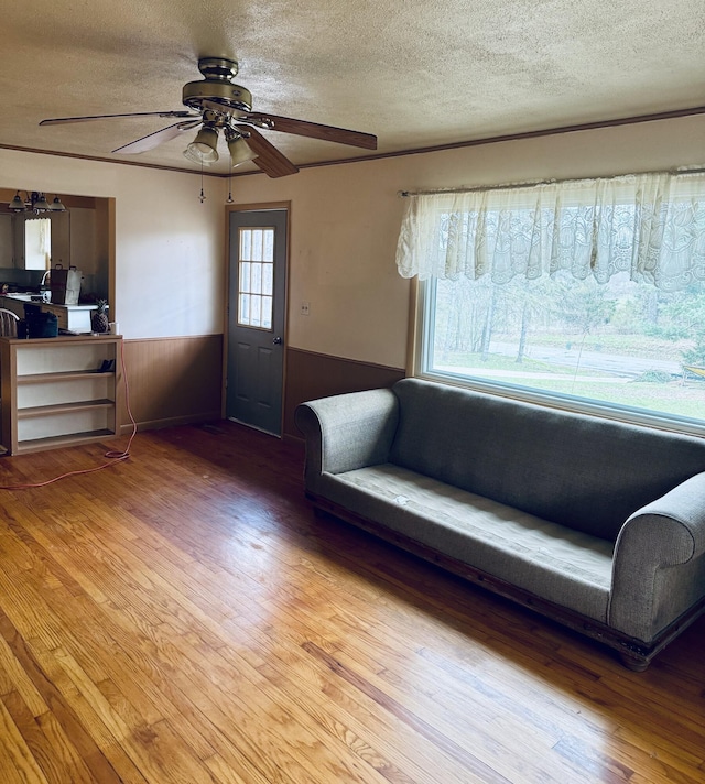 unfurnished living room featuring light wood-style flooring, a textured ceiling, ceiling fan, and wainscoting