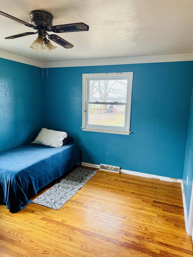 bedroom with baseboards, wood finished floors, visible vents, and ceiling fan