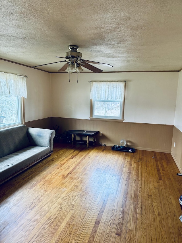 living room featuring a wainscoted wall, wood finished floors, a textured ceiling, and ceiling fan