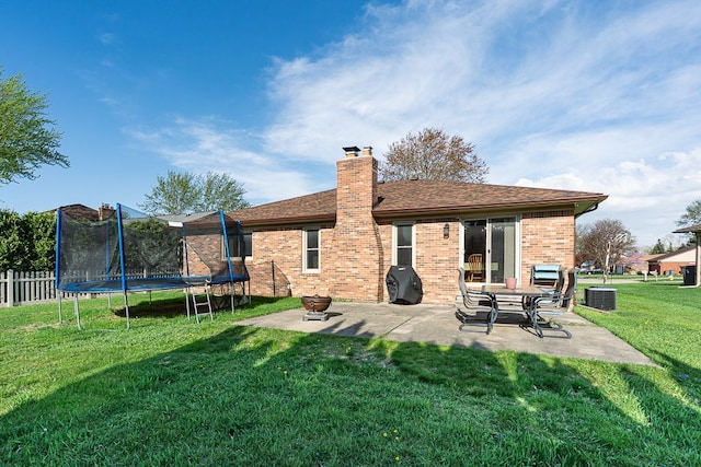 rear view of house featuring a patio, a trampoline, a chimney, a lawn, and brick siding