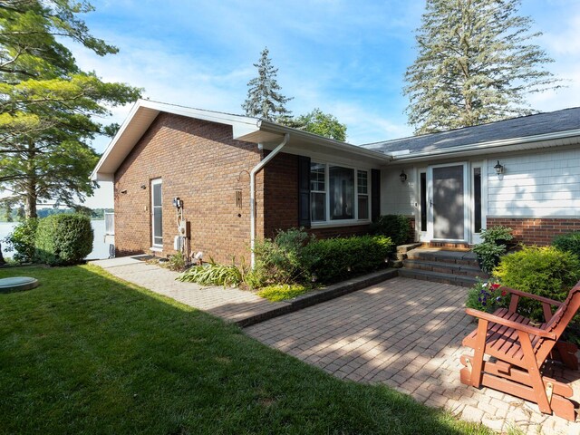 back of house featuring entry steps, brick siding, a yard, and a patio
