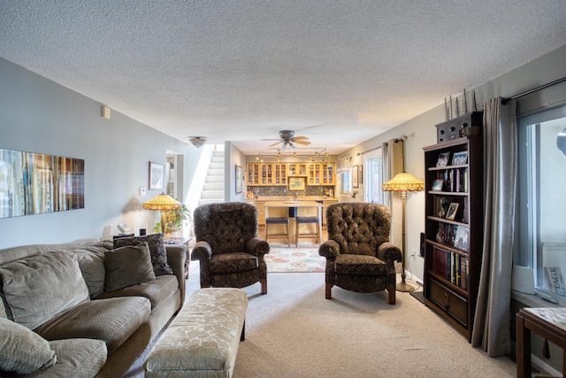carpeted living room with a ceiling fan, a textured ceiling, and stairs