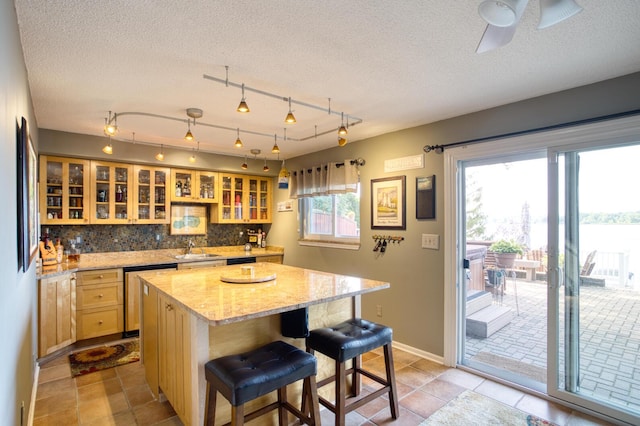 kitchen featuring a kitchen breakfast bar, stainless steel dishwasher, a sink, a kitchen island, and decorative backsplash