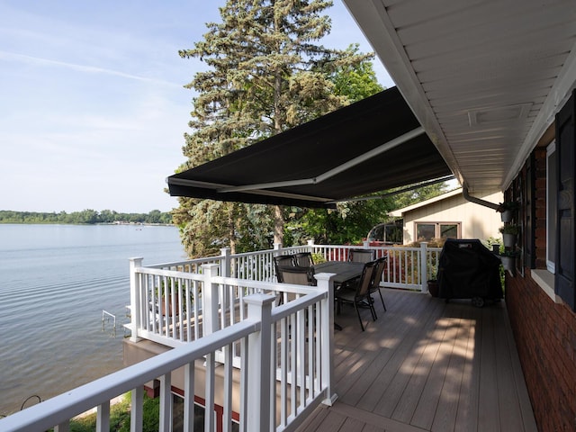 deck featuring outdoor dining space, a water view, and a grill