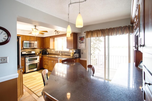 kitchen with stainless steel appliances, a textured ceiling, a sink, backsplash, and brown cabinets