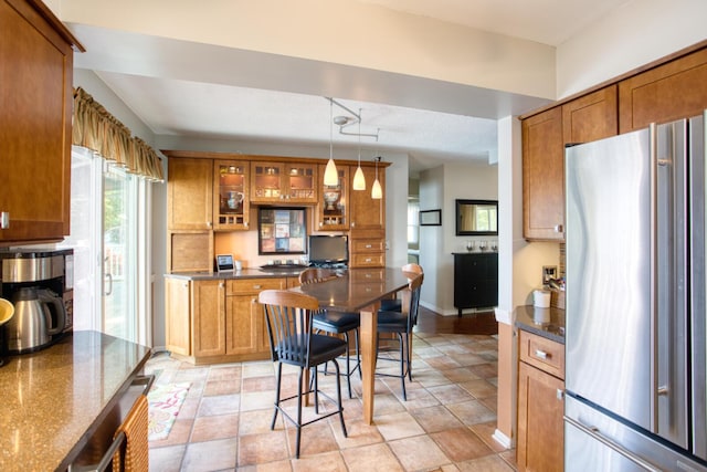 kitchen featuring brown cabinetry, glass insert cabinets, pendant lighting, baseboards, and freestanding refrigerator