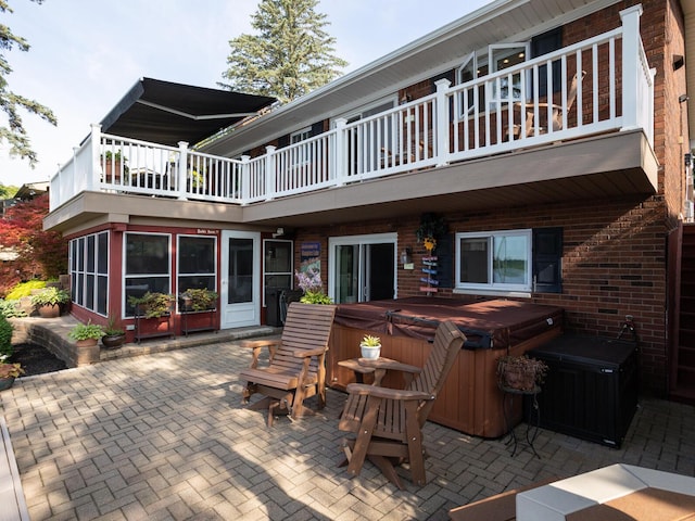 rear view of house with brick siding, a hot tub, a patio area, and a balcony