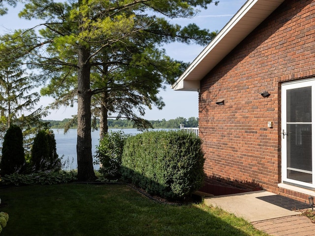 view of side of property with brick siding, a yard, and a water view