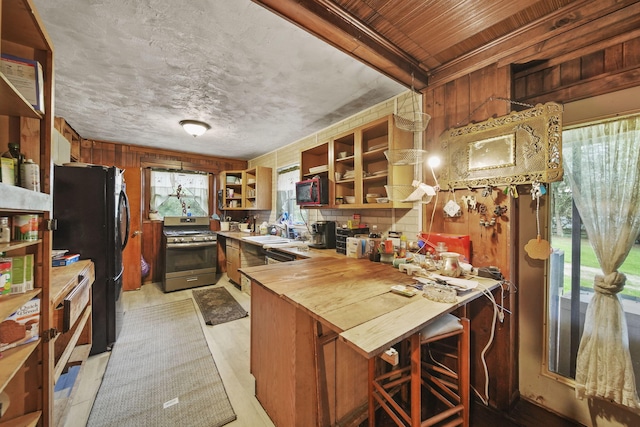 8825 Mills Rd, Manitou Beach, MI 49253 - kitchen with stainless steel gas stove, open shelves, freestanding refrigerator, a peninsula, and wooden counters