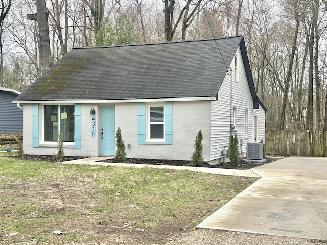 view of front of house with brick siding, a shingled roof, central AC unit, and fence