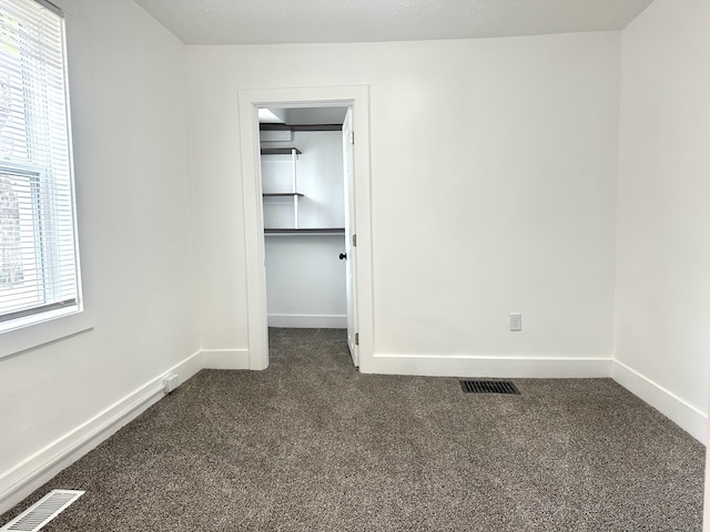 unfurnished bedroom featuring baseboards, visible vents, dark carpet, and a walk in closet