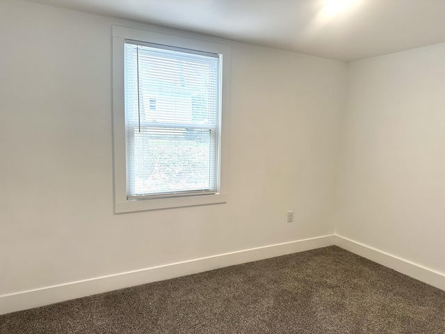 unfurnished room featuring baseboards and dark carpet