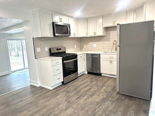 kitchen with tasteful backsplash, a sink, light countertops, dark wood finished floors, and appliances with stainless steel finishes