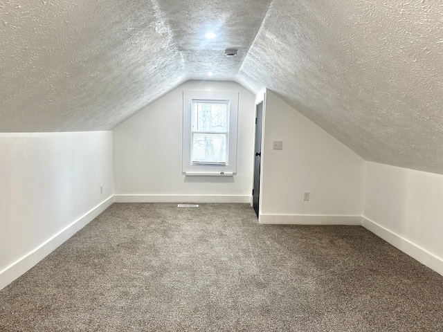 additional living space with vaulted ceiling, a textured ceiling, baseboards, and carpet