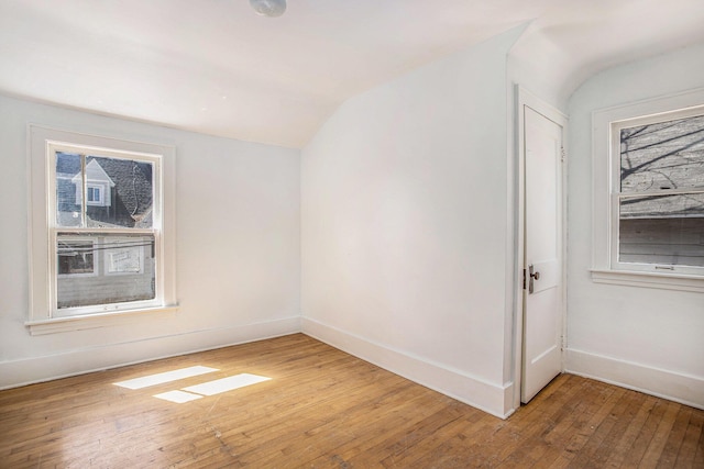 spare room featuring light wood-style floors, vaulted ceiling, and baseboards