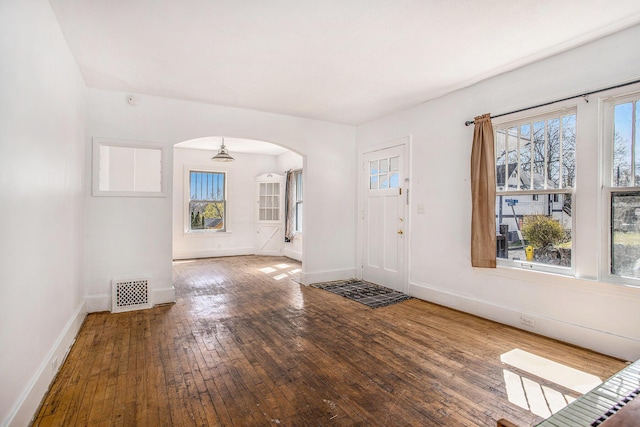 entryway with arched walkways, wood-type flooring, visible vents, and baseboards