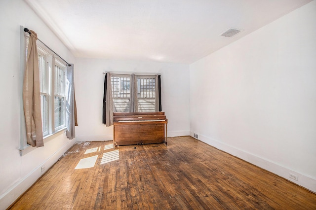 unfurnished room featuring baseboards, visible vents, and hardwood / wood-style flooring