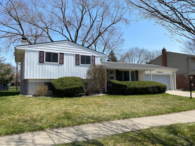 tri-level home with a chimney, brick siding, an attached garage, board and batten siding, and a front yard