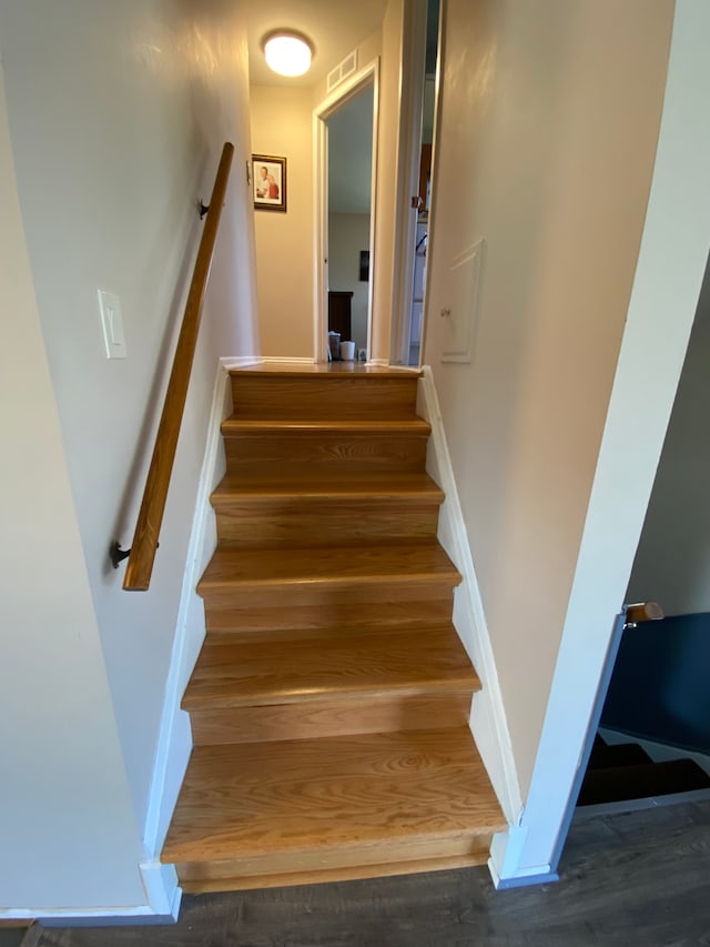 staircase featuring baseboards, wood finished floors, and visible vents