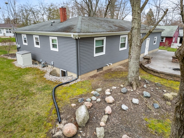 view of side of home featuring a chimney, roof with shingles, a patio, and a lawn