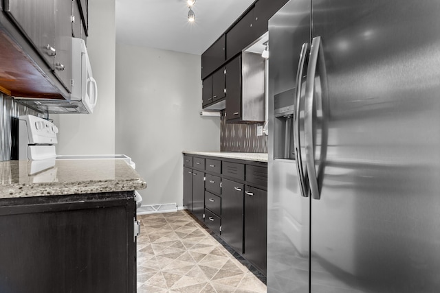 kitchen with light stone counters, white microwave, baseboards, stainless steel refrigerator with ice dispenser, and stove