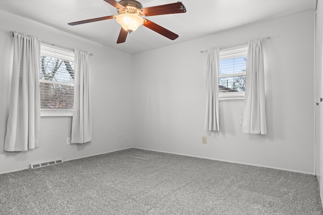 carpeted spare room with baseboards, visible vents, a wealth of natural light, and ceiling fan