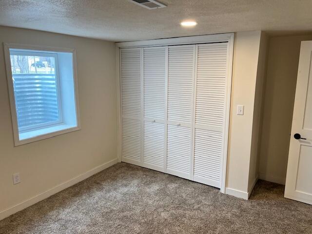 unfurnished bedroom featuring a textured ceiling, carpet, a closet, and visible vents