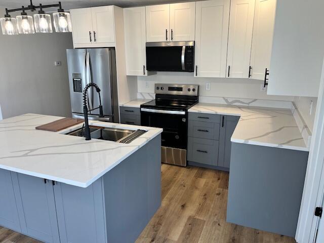 kitchen with light stone countertops, light wood-style flooring, decorative light fixtures, and appliances with stainless steel finishes