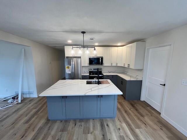 kitchen with light stone counters, appliances with stainless steel finishes, light wood-style floors, and a kitchen island with sink