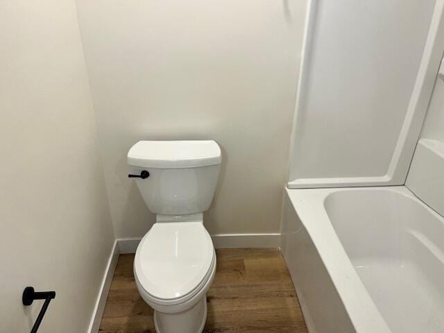 bathroom featuring wood finished floors, toilet, baseboards, and a bathtub