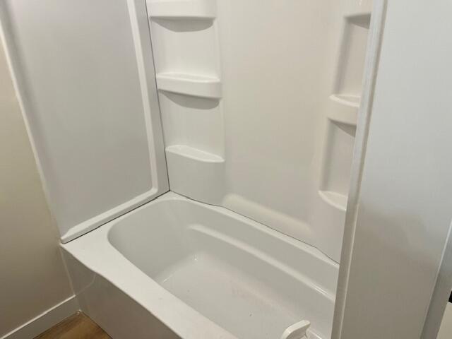 bathroom featuring walk in shower, a washtub, and baseboards