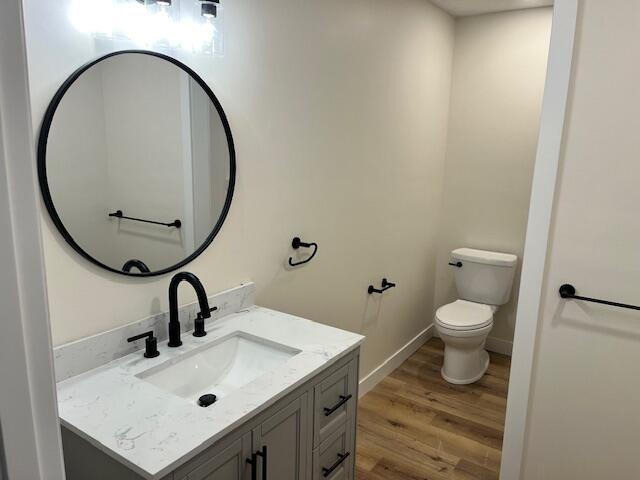 half bathroom featuring baseboards, wood finished floors, vanity, and toilet