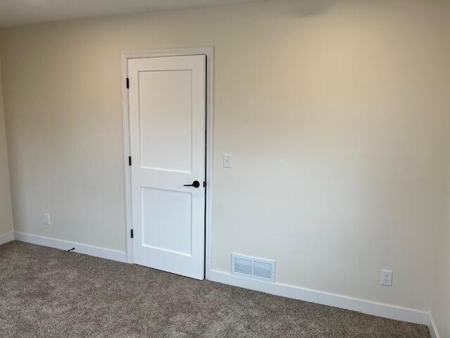 unfurnished room with carpet, visible vents, and baseboards