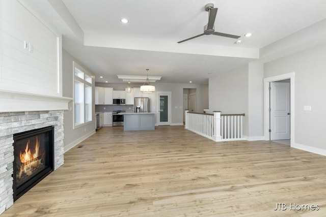 7571 Brook Villa Ct, Allendale, MI 49401 - unfurnished living room with ceiling fan, a fireplace, recessed lighting, a tray ceiling, and light wood-style flooring