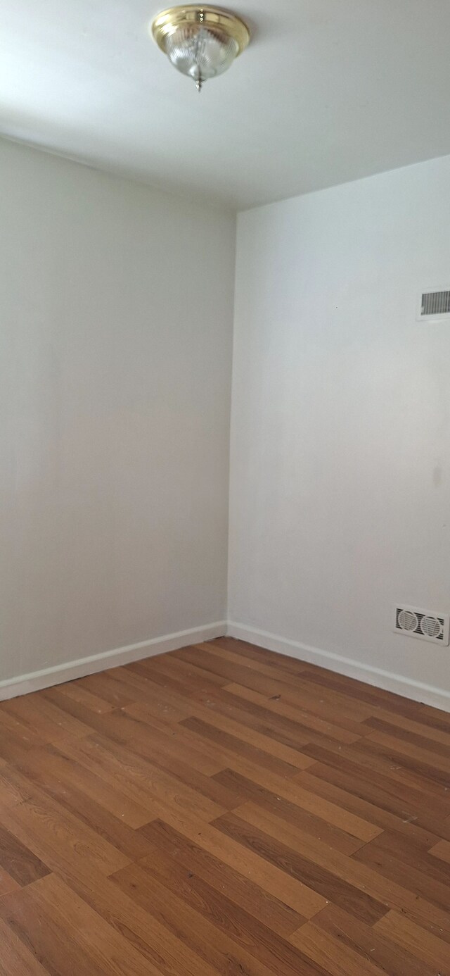 empty room featuring baseboards, wood finished floors, and visible vents